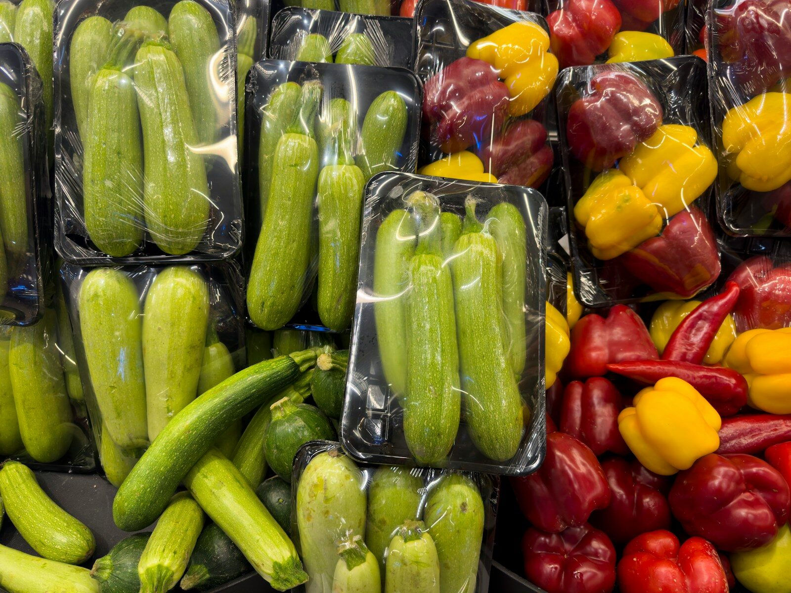 Fresh zucchini and bell peppers packaged for sale.